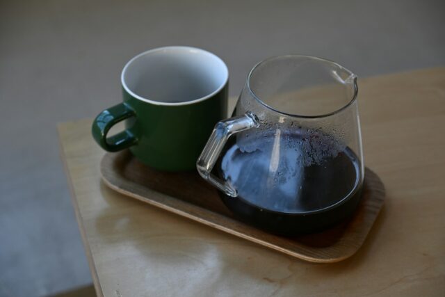 A green mug and a glass coffee carafe on a tray
