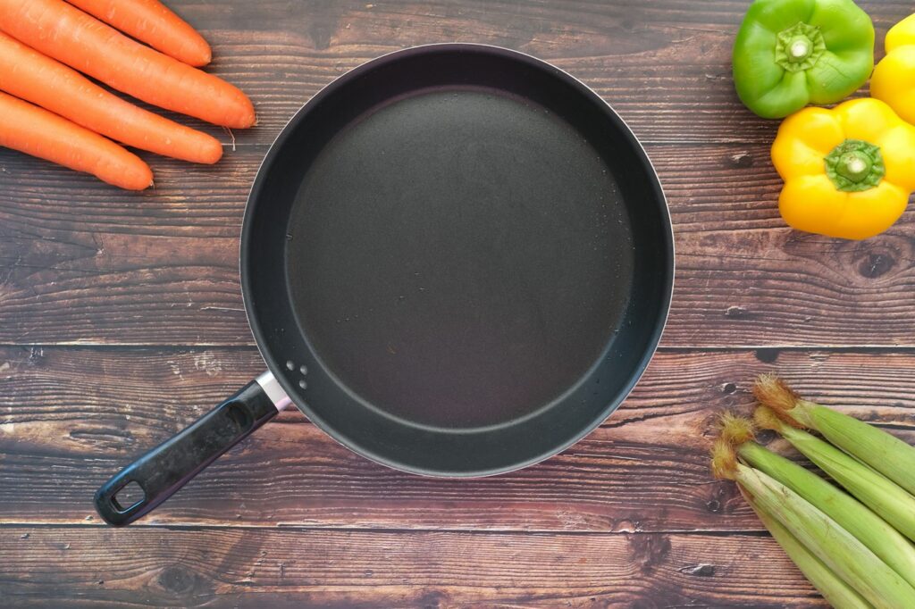 Empty frying pan beside vegetables on a kitchen work surface